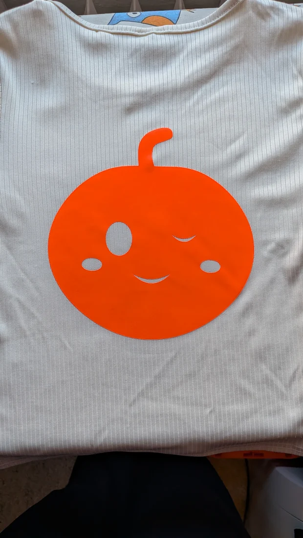 Großes oranges Kürbis-Bügelbild mit zwinkerndem Gesicht auf hellem Shirt